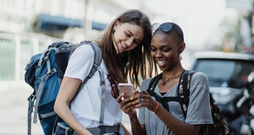 Happy Girls Travelers with Backpacks Using Mobile