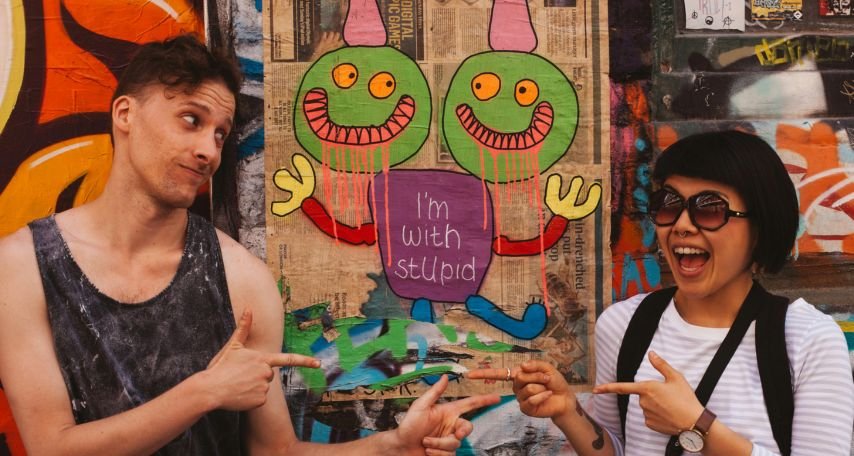 Man on Black Tank Top Pointing at Woman on White Long Sleeve Top
