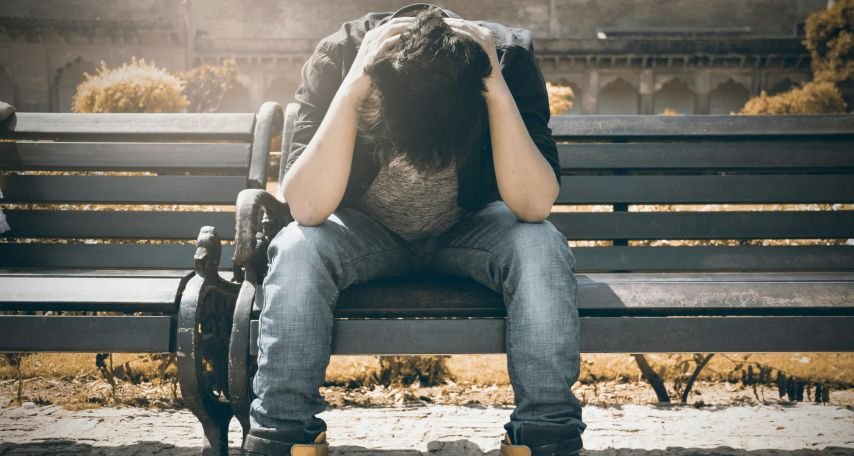 Man in Black Shirt and Gray Denim Pants Sitting on Gray Padded Bench