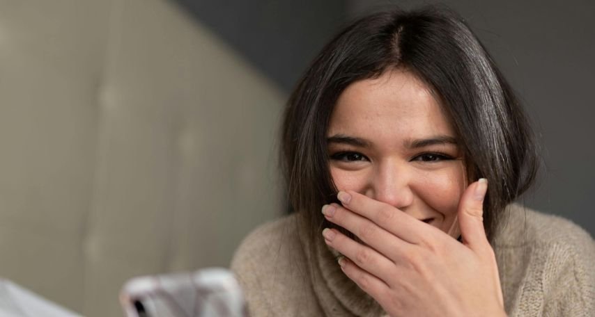 Young woman smiling while browsing smartphone on bed