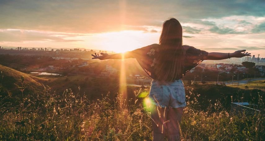 Woman Stands on Mountain over Field Under Cloudy Sky at Sunrise