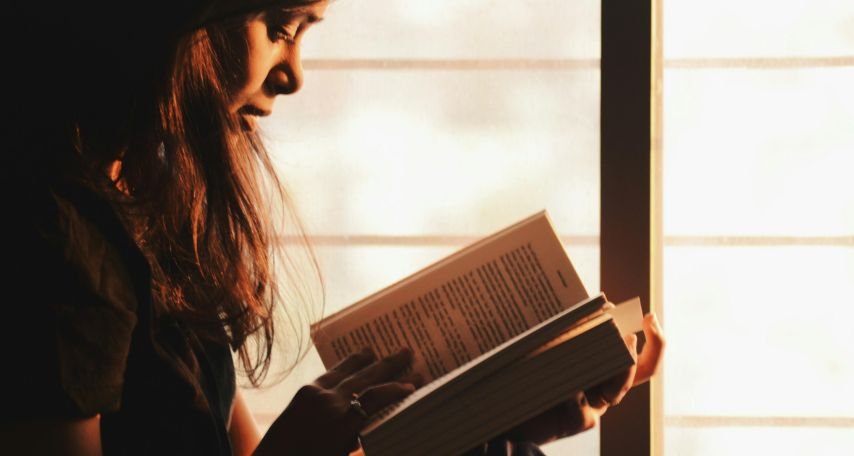 Woman Reading a Book Beside the Window