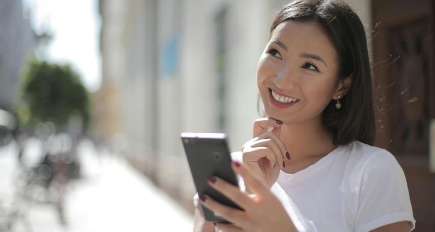 Smiling Woman in White Shirt Holding Smartphone
