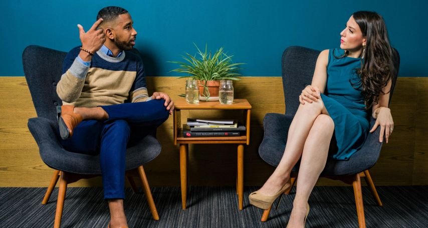 Woman Wearing Teal Dress Sitting on Chair Talking to Man