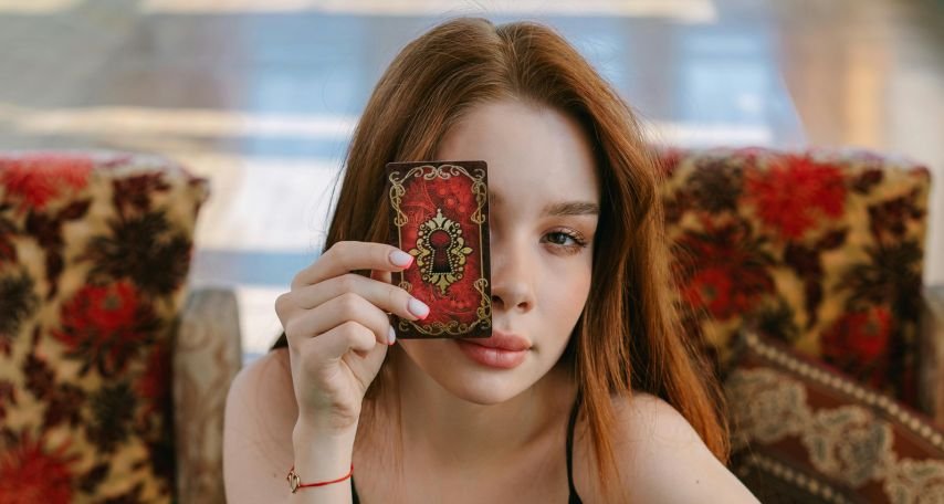 A Woman in Black Tank Top Holding a Tarot Card while Covering Her One Eye