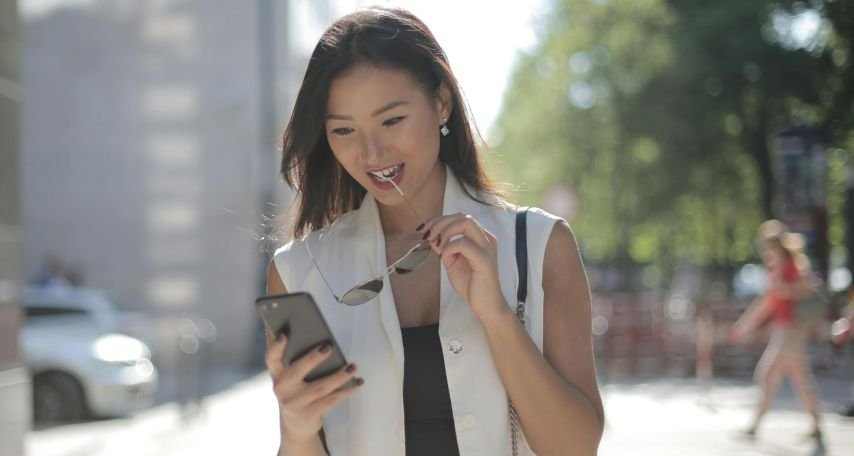 Woman in White Sleeveless Dress Holding Black Smartphone smiling
