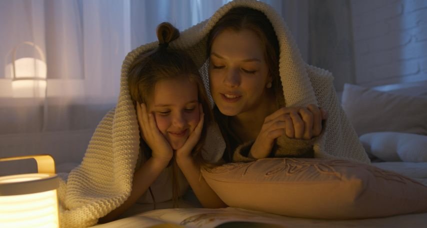 Mother and Daughter Lying on Bed while Reading a Book
