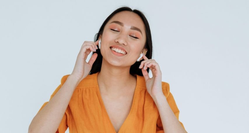 A Happy Woman in Orange Dress Listening to Music on her Wireless Earphones