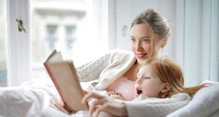 Mother and daughter reading book with interest in bed
