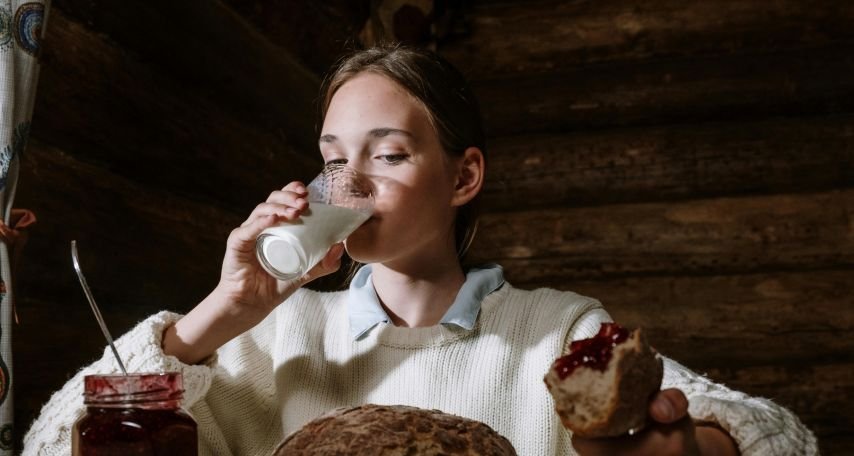 Girl Sitting at the Table and Eating Bread with Jam and Drinking Milk
