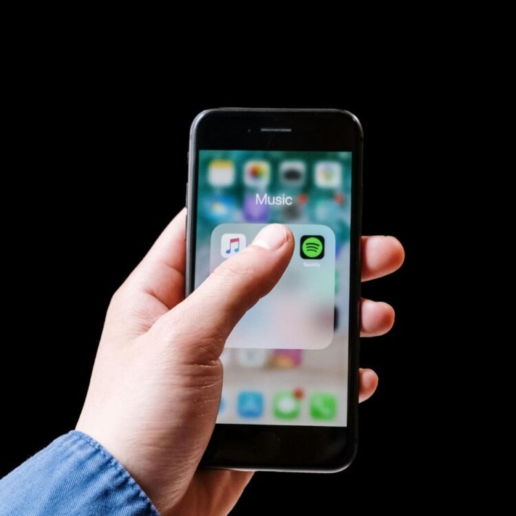 Person Holding an Iphone With Apple Music and Spotify app Display