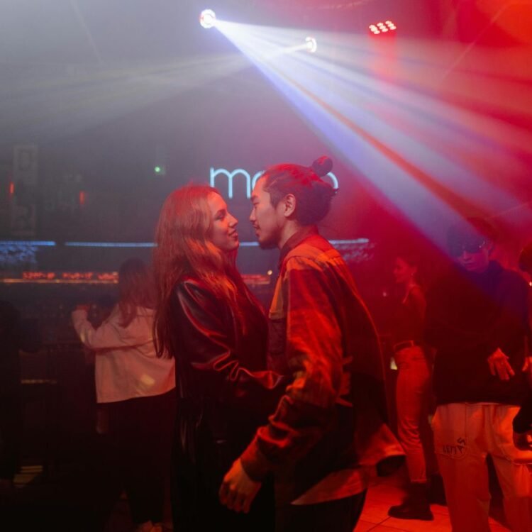 A woman in leather jacket holding a guy in a club