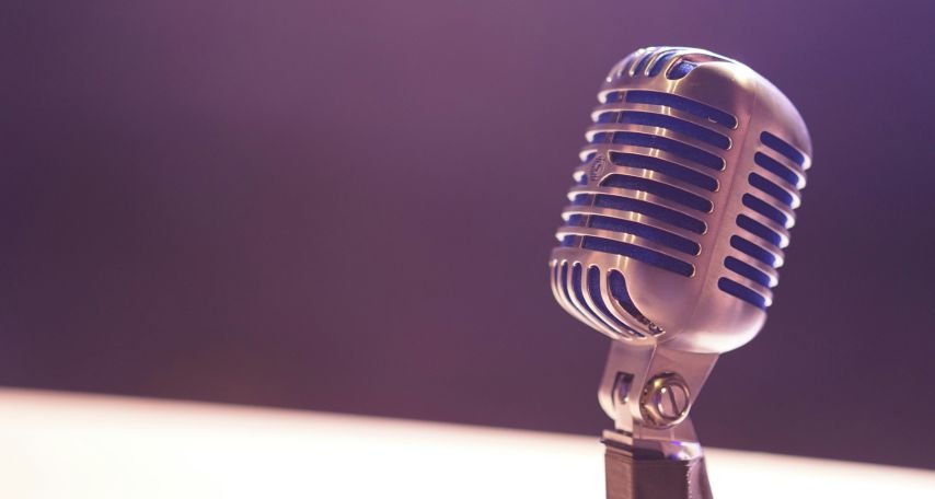 Vintage mic under stage lights, hinting at a legendary return.