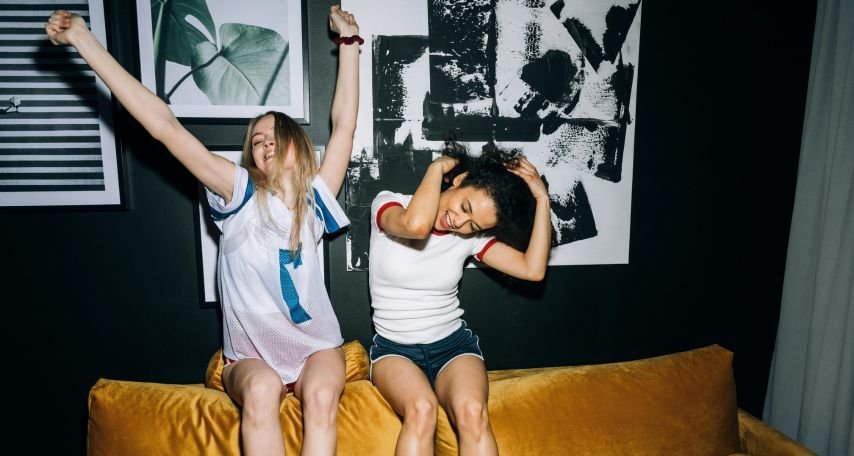 Two Young Women Having Fun While Sitting on a Yellow Sofa