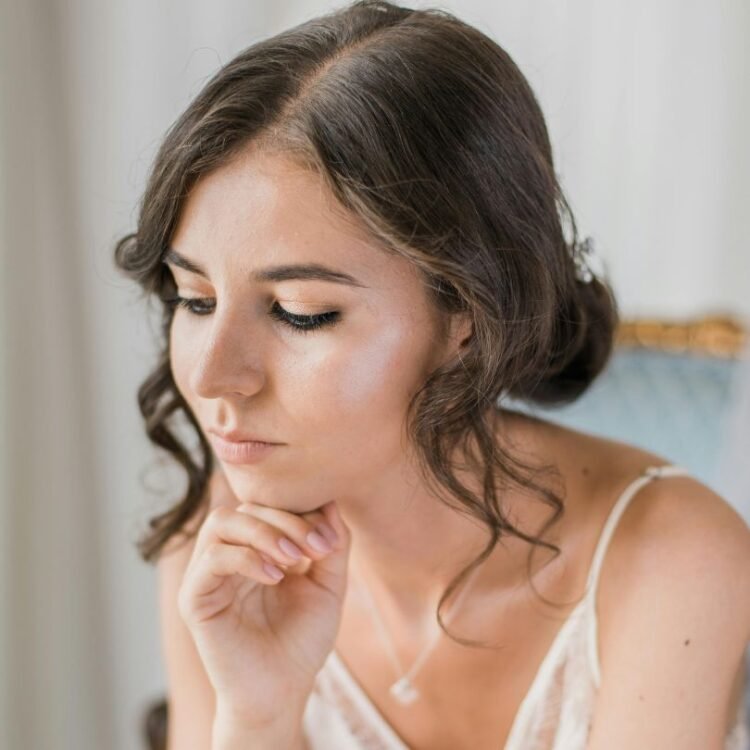 Woman in a white top resting her chin on her hand, appearing thoughtful.